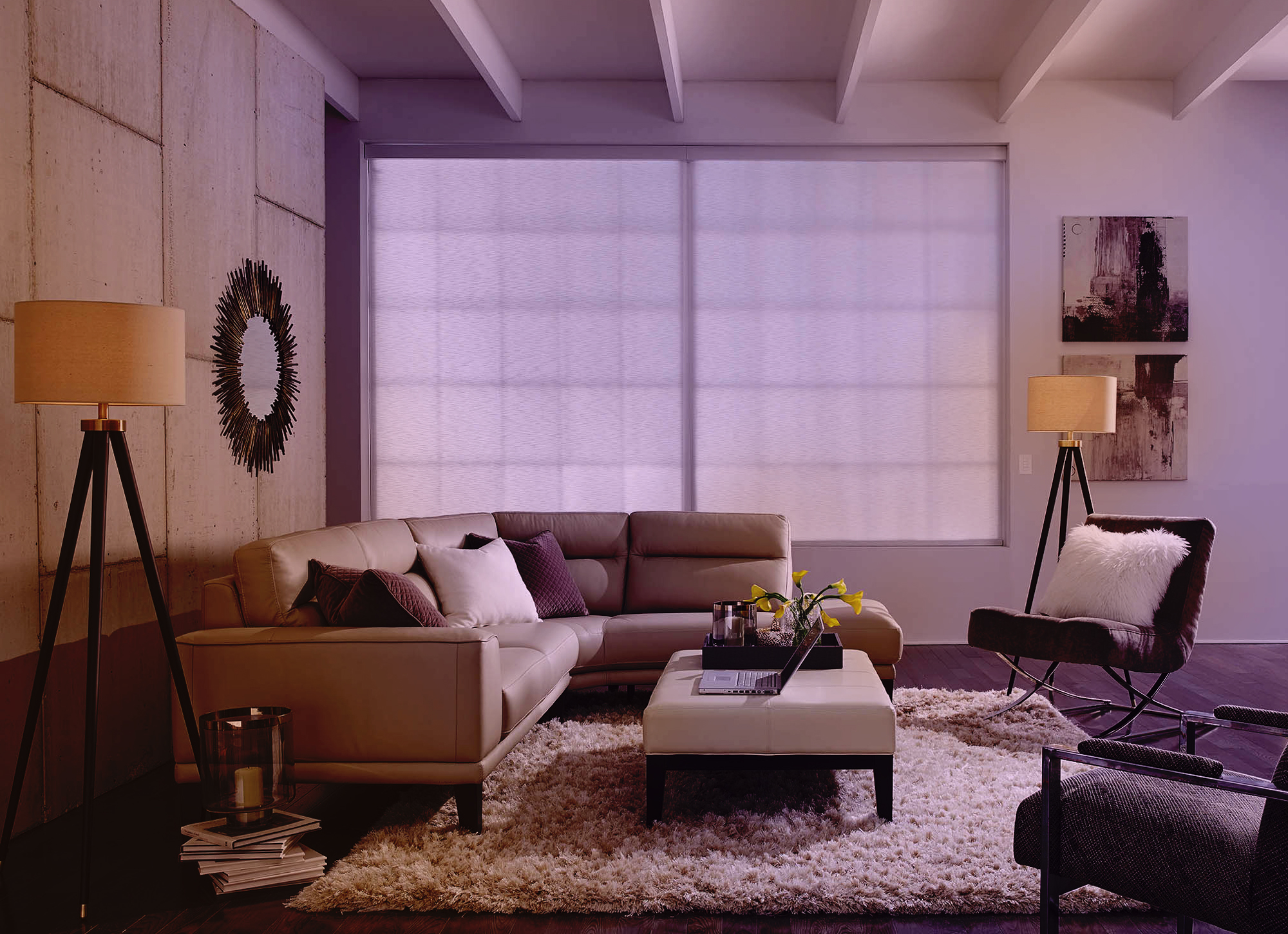 A living room scene bathed in soft evening light: the sofa and ottoman are illuminated with a warm glow, the roller shades appear gently backlit, and the floor lamps cast cozy pools of light for a relaxed, entertaining atmosphere.